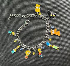 the simpsons character charm bracelet is shown on a black surface with other cartoon characters around it