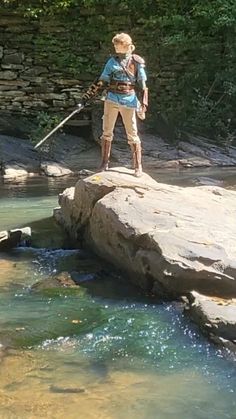 a man standing on top of a rock next to a small river filled with water