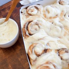 a pan filled with cinnamon rolls next to a small bowl of cream cheese frosting