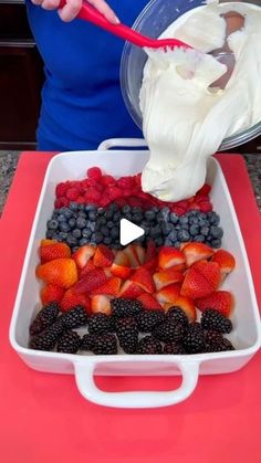 a woman is pouring fruit into a white dish with whipped cream on top and berries in the bottom