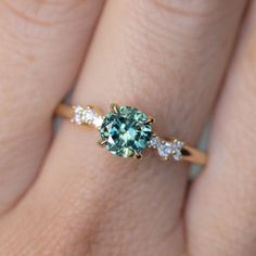 a woman's hand holding a ring with a green and white diamond in it