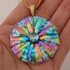 a hand holding a colorful glass pendant in it's palm