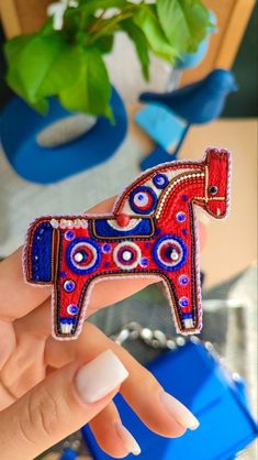 a hand holding a red and blue horse brooch