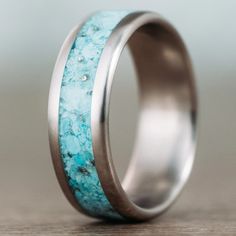 a wedding band with turquoise and silver inlaying the center, on a wooden table