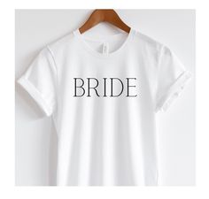 a white t - shirt with the word bride printed on it, hanging from a wooden hanger