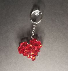 a red heart shaped keychain hanging from a metal hook on a gray surface