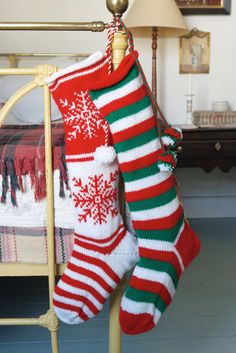 two knitted christmas stockings hanging from a wooden pole in front of a gold bed