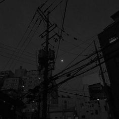 telephone poles and wires at night with the moon in the sky over buildings behind them