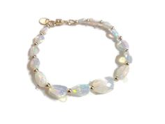 This opal bracelet created by Jewelry by CARMAL is made of nugget natural Ethiopian opal gemstones, 14k gold: beads, and magnetic clasp closure. This bracelet measures 7 1/2 inches in length and is finished with at 14k gold oval charm.  The pictures do not do this bracelet justice! This bracelet would go great with these earrings: https://www.etsy.com/listing/1530862840/ethiopian-opal-earrings-october?click_key=ff8af590c11569fc9ae2a12061e1d30023f83387%3A1530862840&click_sum=89e7b0ab&ga_search_qu Formal Adjustable Iridescent Jewelry, Elegant Crystal Bracelet With Gemstone Beads And Moonstone, Elegant White Faceted Beaded Bracelets, Elegant White Beaded Bracelets With Gemstones, Elegant White Gemstone Beaded Bracelets, Elegant White Beaded Gemstone Bracelets, Elegant Handmade White Gemstones, Elegant Opal Jewelry With Gemstone Beads, Elegant White Faceted Bracelets