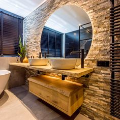 a bathroom with two sinks and a large round mirror over the sink, in front of a brick wall