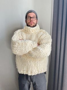 a man with glasses and a sweater is standing in front of a window, arms crossed