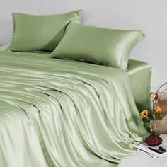 a bed covered in green sheets and pillows with flowers on the nightstand next to it