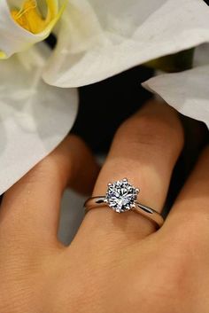 a woman's hand with a diamond ring on it and flowers in the background