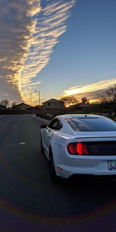 a white car parked on the side of a road under a cloudy blue sky with wispy clouds