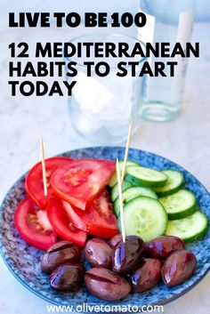 a blue plate topped with cucumbers, tomatoes and olives next to a glass of water