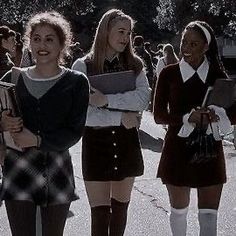 three girls in school uniforms are standing on the street