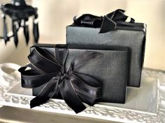 two black wrapped presents sitting on top of a white tray with ribbon around the edges