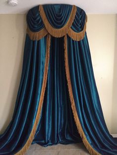 a large blue curtain with gold fringes hanging from it's sides in front of a white wall