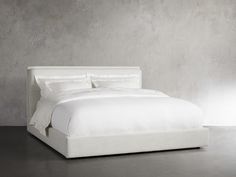 a bed with white linens and pillows in a gray room next to a concrete wall