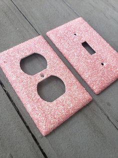 two pink glittered switch plates sitting on top of a wooden floor next to each other