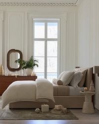 a bedroom with white walls and wooden floors has a bed, dresser, chair, mirror and potted plant in the corner