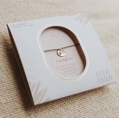 a white box with a gold charm on it sitting on a beige cloth covered surface