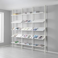 a white shelving unit with books on it in an empty room next to a window