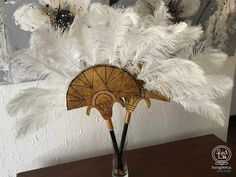 a vase filled with white feathers on top of a wooden table next to a wall