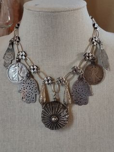 An assemblage of ethnic silver elements featuring a 925 sterling Yemeni amulet with the makers mark, possibly made by a Jewish Bawsani silversmith. I've flanked it with silver Turkmen pendulum shaped pendants, two walking liberty coin pendants from a Navajo squash blossom necklace, and Moroccan Berber Hamsa in two styles. All elements are suspended from triple plated silver chain. Finishes with a silver plated hook. Artisan Silver Engraved Necklaces, Artisan Oxidized Finish Jewelry For Festivals, Artisan Jewelry With Oxidized Finish For Festivals, Sterling Silver Amulet Necklace With Oxidized Finish, Artisan Sterling Silver Necklace For Festival, Spiritual Antique Silver Nickel-free Jewelry, Nickel-free Antique Silver Jewelry, Traditional Sterling Silver Nickel Free Necklace, Antique Silver Medallion Necklace In Sterling Silver