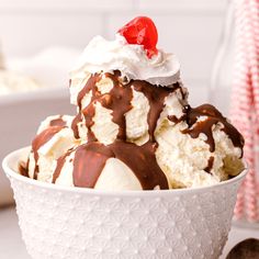 an ice cream sundae with chocolate sauce and cherries in a white bowl on a table