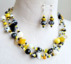 Make a real statement with this OOAK colorful necklace set. Both vintage and new glass beads, lamp work glass, jade stones, agate stones, ceramic beads, and resin beads in hues of yellow, gold, white and black are all strung on 3 wires and finished with decorative silver bead caps, a stainless-steel chain, and a large lobster clasp.  Necklace finished length is 16 inches long with an additional chain measuring 4 inches, for comfort. Matching lampwork glass beaded earrings are hung on 925 silver ear wires. Unique Yellow Jewelry With Gemstone Beads, Yellow Czech Glass Jewelry With Colorful Beads, Unique Yellow Czech Glass Jewelry, Handmade Yellow Czech Glass Beaded Necklaces, Handmade Yellow Beaded Necklace With Czech Glass, Handmade Yellow Czech Glass Necklace, Yellow Czech Glass Beaded Necklaces For Jewelry Making, Bumble Bee Necklace, Black Beaded Necklace