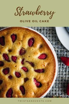 a strawberry olive oil cake on a table with strawberries around it and text overlay that reads, strawberry olive oil cake