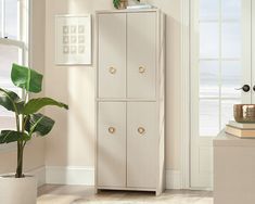 a tall white cabinet sitting in a living room next to a plant on top of a table