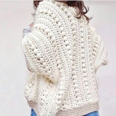 a woman is wearing a white crochet sweater and blue jeans with her hands in her pockets