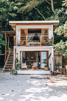 a small white house sitting on top of a beach next to some trees and bushes