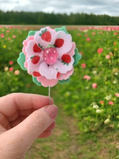 a hand holding a strawberry flower on top of a green field