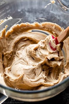 a mixing bowl filled with peanut butter on top of a counter next to a wooden spoon