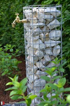 a bird feeder made out of rocks in the middle of some bushes and trees with water running from it's faucet