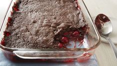 a chocolate cake with cherries in a glass baking dish on a blue towel next to a spoon