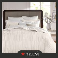 a bed with white sheets and pillows in a bedroom next to a window that says macy's