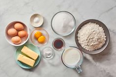 an assortment of ingredients are shown in bowls on a marble countertop, including eggs, butter, flour, and milk