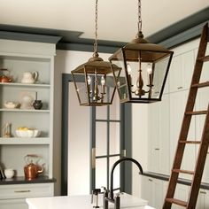 two lights hanging over a kitchen sink next to a ladder in a room with white cabinets