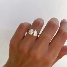 a woman's hand holding a three stone diamond ring in her left hand, with the other hand on it