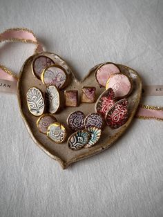 a heart shaped box filled with lots of different types of buttons on a white surface