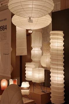 many white paper lanterns hanging from the ceiling in a room with chairs and lamps around them