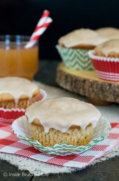 two muffins with icing on top sitting on napkins next to a jar of orange juice