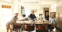 a group of people standing around a kitchen table with chairs and an oven in the background