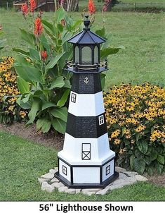 a black and white lighthouse sitting on top of a lush green field next to flowers