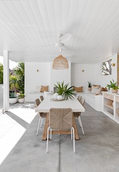 a dining room with white walls and ceiling fan in the center, surrounded by plants