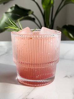 a pink glass with ice cubes in it on a marble table next to a potted plant